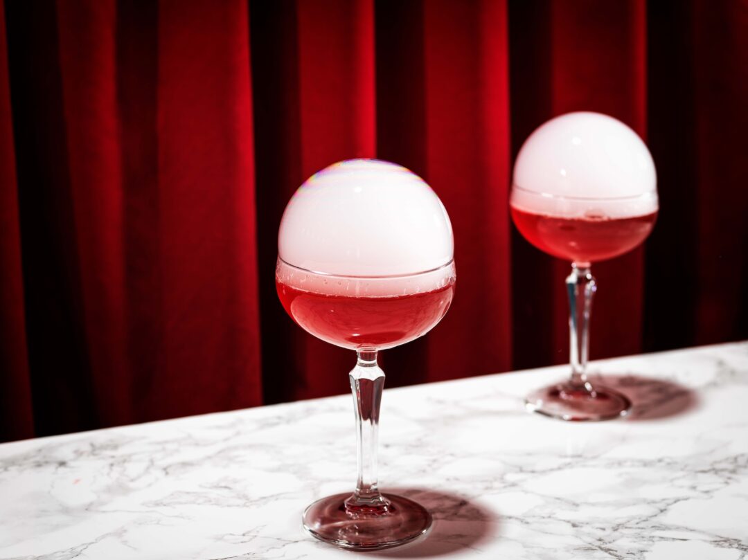 bildstadt Foodfotografie – Kenny Klein Cocktails - roter Cocktail mit Rauchblase mit rotem Vorhang in Hintergrund