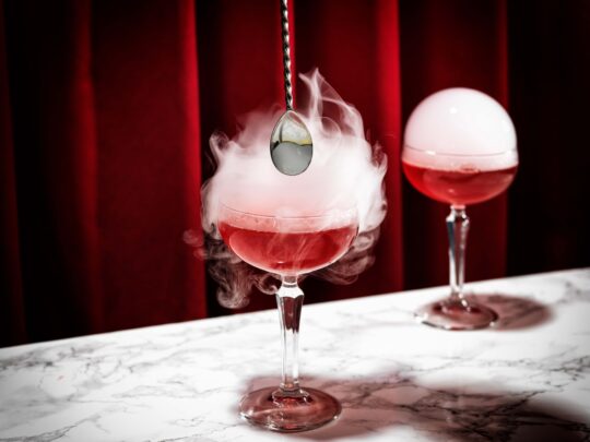 bildstadt Foodfotografie – Kenny Klein Cocktails - roter Cocktail mit platzender Rauchblase und rotem Vorhang in Hintergrund